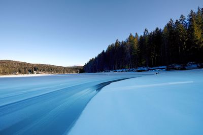 Snow covered road by trees against clear blue sky