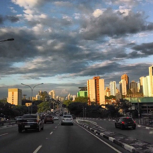 car, transportation, building exterior, architecture, land vehicle, built structure, city, road, sky, mode of transport, street, cloud - sky, traffic, city life, cloudy, city street, skyscraper, road marking, cloud, cityscape