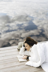 Young woman reading book while lying on pier