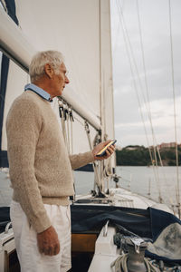 Senior man navigating direction through smart phone while standing on boat during sunset