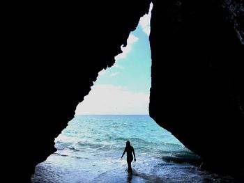 Silhouette man on rock formation by sea against sky