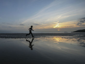 Reflection of woman jogging on water at beach against sky