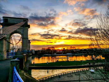 Bridge over river against cloudy sky during sunset