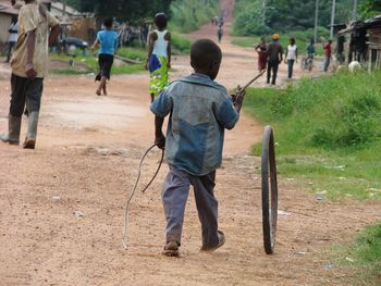 Rear view of boy playing with tire while walking on field