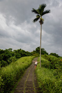Woman standing on footpath against cloudy sky