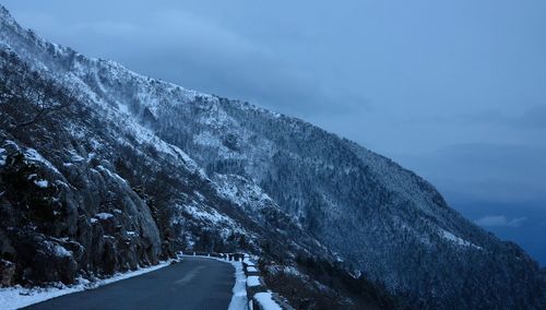 Snow covered road by mountain against sky