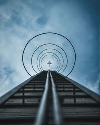 Low angle view of metallic structure against sky with an airplane