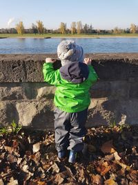 Rear view of boy standing by retaining wall against river
