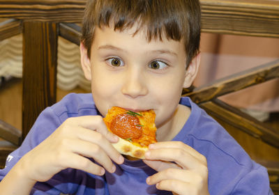 Boy eating pizza. child closed his eyes in pleasure and takes a bite of pizza piece holding it aloft