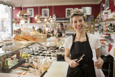 Portrait of happy saleswoman cutting cheese at counter in supermarket