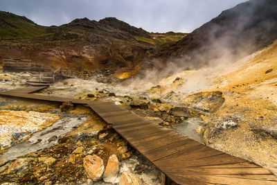 Boardwalk leading towards hot spring against sky