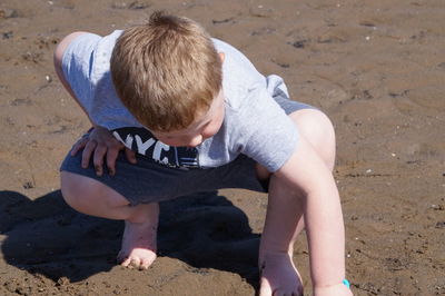 Full length of boy crouching on sand at beach