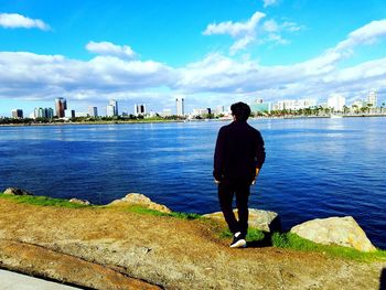 Full length rear view of man walking on river against cityscape