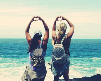 Rear view of women forming heart shapes with hand at beach