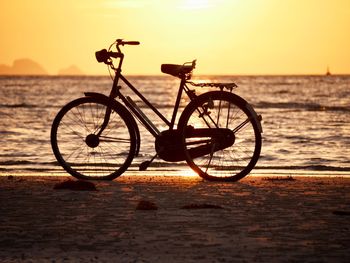 Silhouette bicycle on beach against sky during sunset