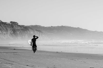 Rear view of man walking with surfboard at beach