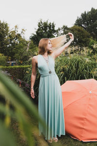 Young woman touching hair while standing against plants