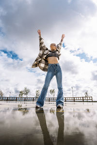 Woman standing with arms raised in front of cloudy sky