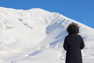 Rear view of person standing on snowcapped mountain against sky