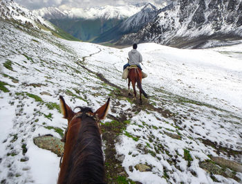 Rear view of man riding horse on snowcapped mountain