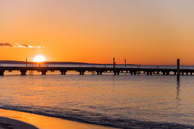 Silhouette bridge over sea against sky during sunset