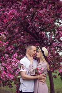 Portrait man and a woman in love stand by a blooming pink cherry tree in summer