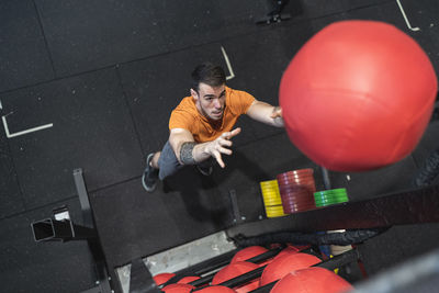 Mid adult man throwing fitness ball while standing in gym