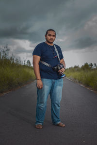 Full length portrait of young man standing on road against sky
