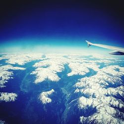 Aerial view of airplane wing over landscape against blue sky