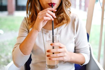 Midsection of woman sipping drink while sitting at restaurant