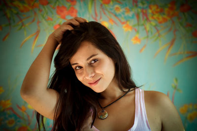 Close-up portrait of young woman with hand in hair standing against patterned wall