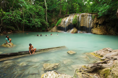 People on rocks by waterfall in forest