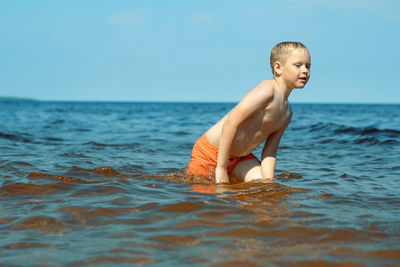 7-8 years old cute caucasian boy going out from the sea to the shore tired.