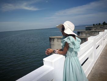 Woman looking at sea while standing by railing against sky