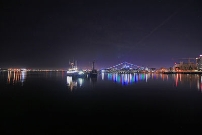 Illuminated city by sea against sky at night