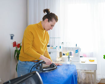 Woman seamstress or housewife ironing fabric before sewing while working at her workplace