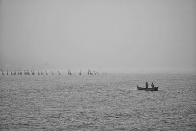 People sailing on boat in sea against sky during foggy weather