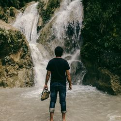 Full length rear view of man standing against waterfall