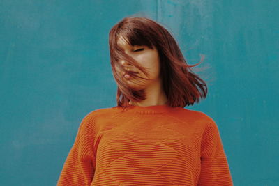 Young woman with closed eyes standing against blue wall