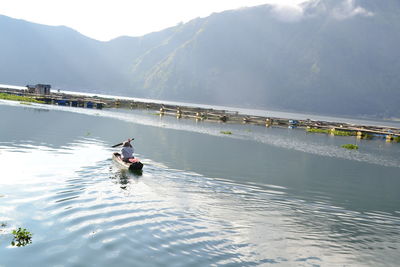 Man rowing boat on lake against sky