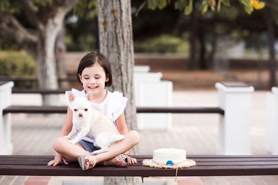 Smiling baby girl 3-4 year old sitting with pet chihuahua in park outdoors. friendship. childhood.