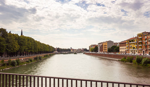 Arch bridge over river amidst buildings in city against sky