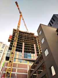 Low angle view of crane by building against sky