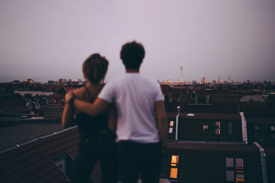 Rear view of couple looking at city while standing on terrace during dusk against sky