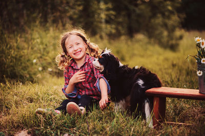 Portrait of happy girl playing with dog while sitting on field