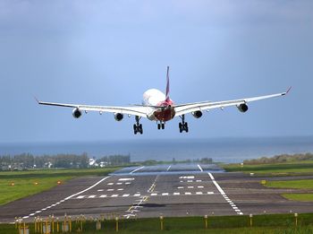 Airplane flying over airport runway against sky