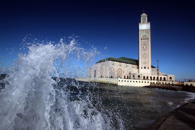 Waves flowing at sea with mosque hassan ii against clear blue sky