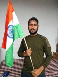 Portrait of young man holding indian flag standing against wall