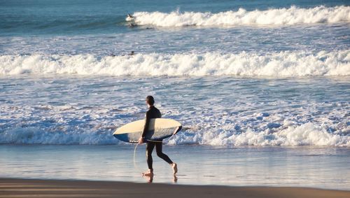 Side view of male surfer walking on beach