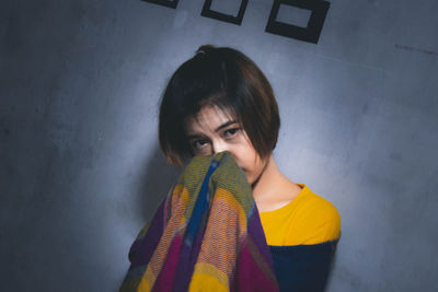 Portrait of young woman with scarf standing against wall